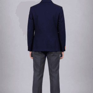 Back side view of Indian school boy wearing navy blue DAV school uniform blazer with grey trousers in studio background
