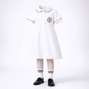 Junior girls DPS-style summer uniform — white tunic with green piping collar, monogram pocket and white socks with green stripes.